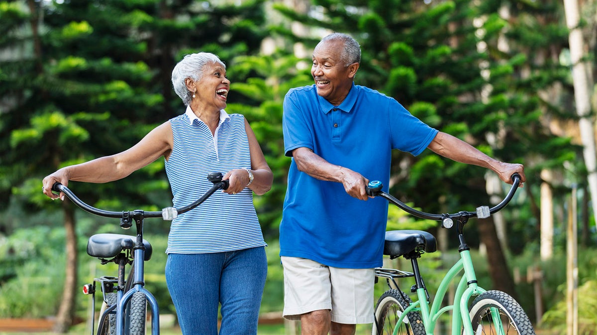 Senior African American couple walk with bikes, laughing