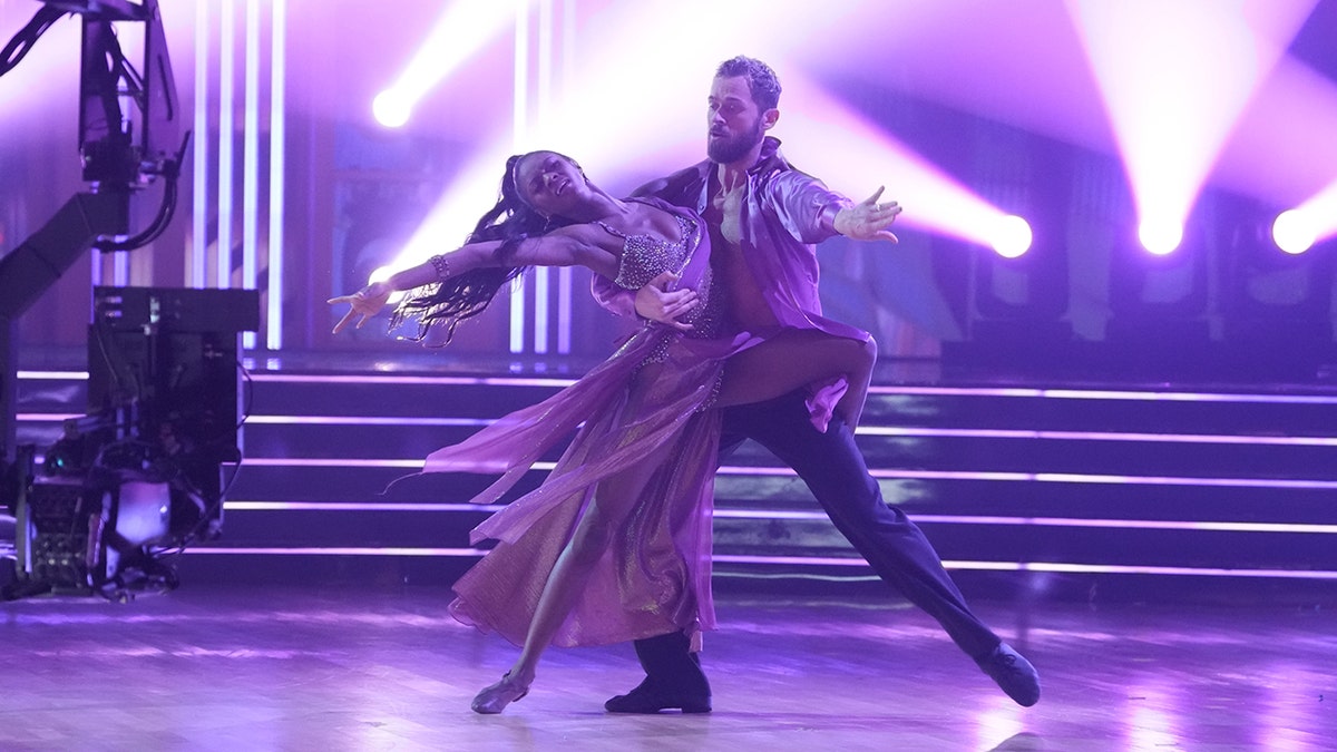 Purple hued picture of Artem Chigvintsev twirling Charity Lawson
