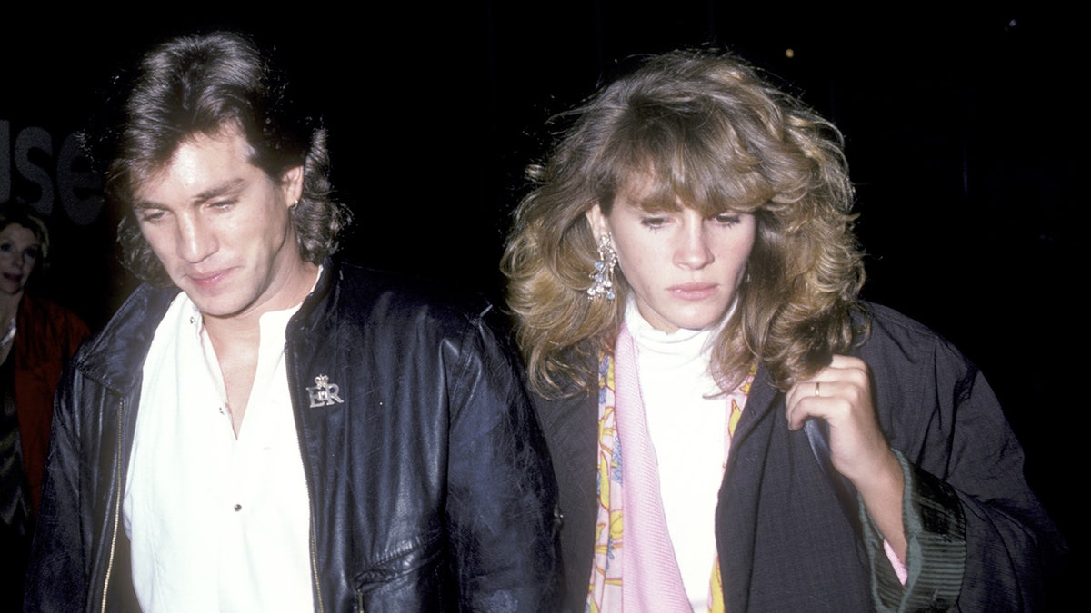 Eric and Julia Roberts, both wearing black coats, walk with their heads partially lowered in 1986