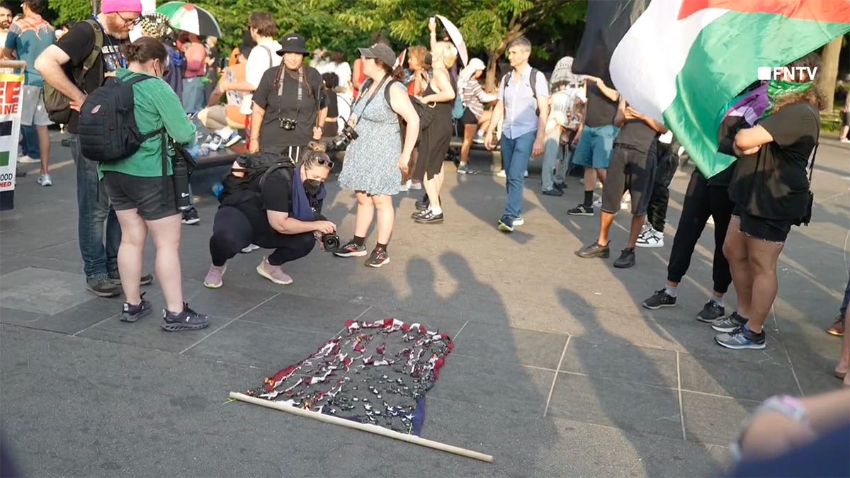 Los espectadores contemplan una bandera estadounidense quemada.