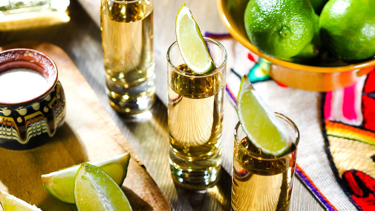 Three shots of tequila in tall shot glasses with lime wedges on top.