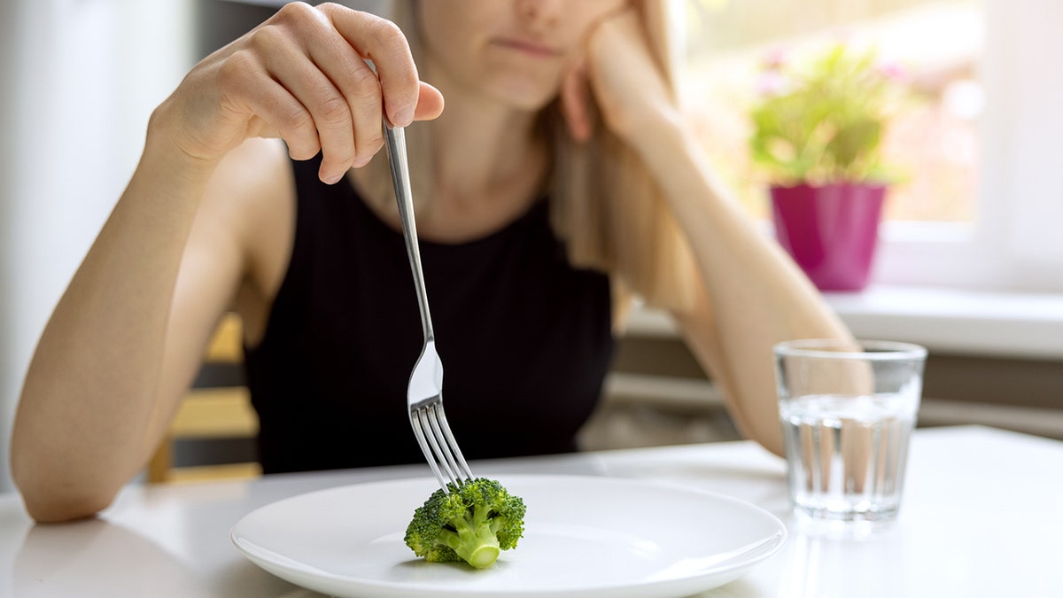 woman looking at small broccoli portion on the plate