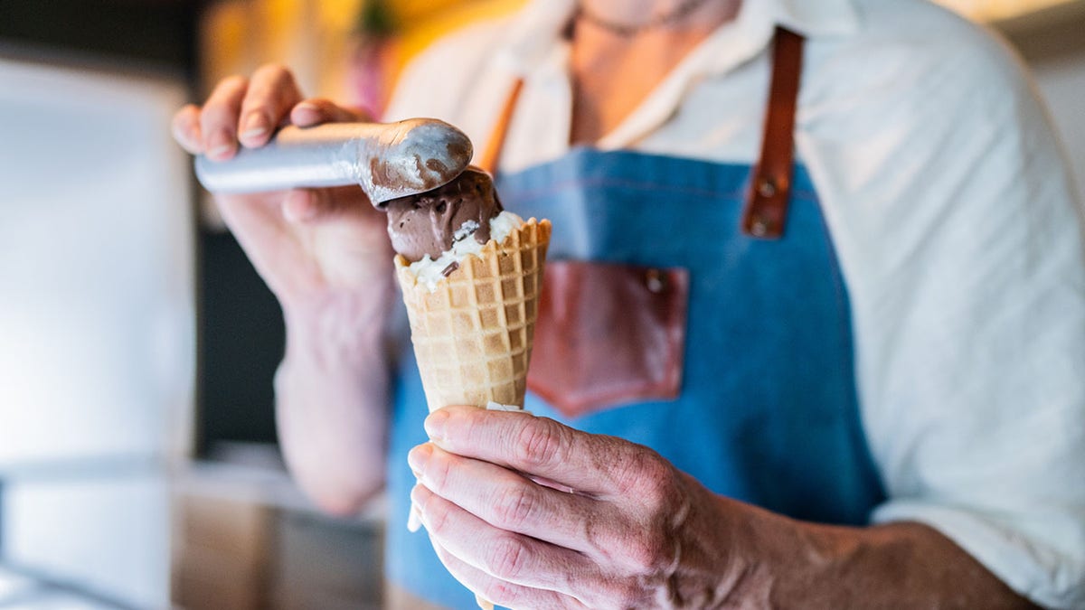 Man scooping a chocolate scoop on top of a vanilla scoop.