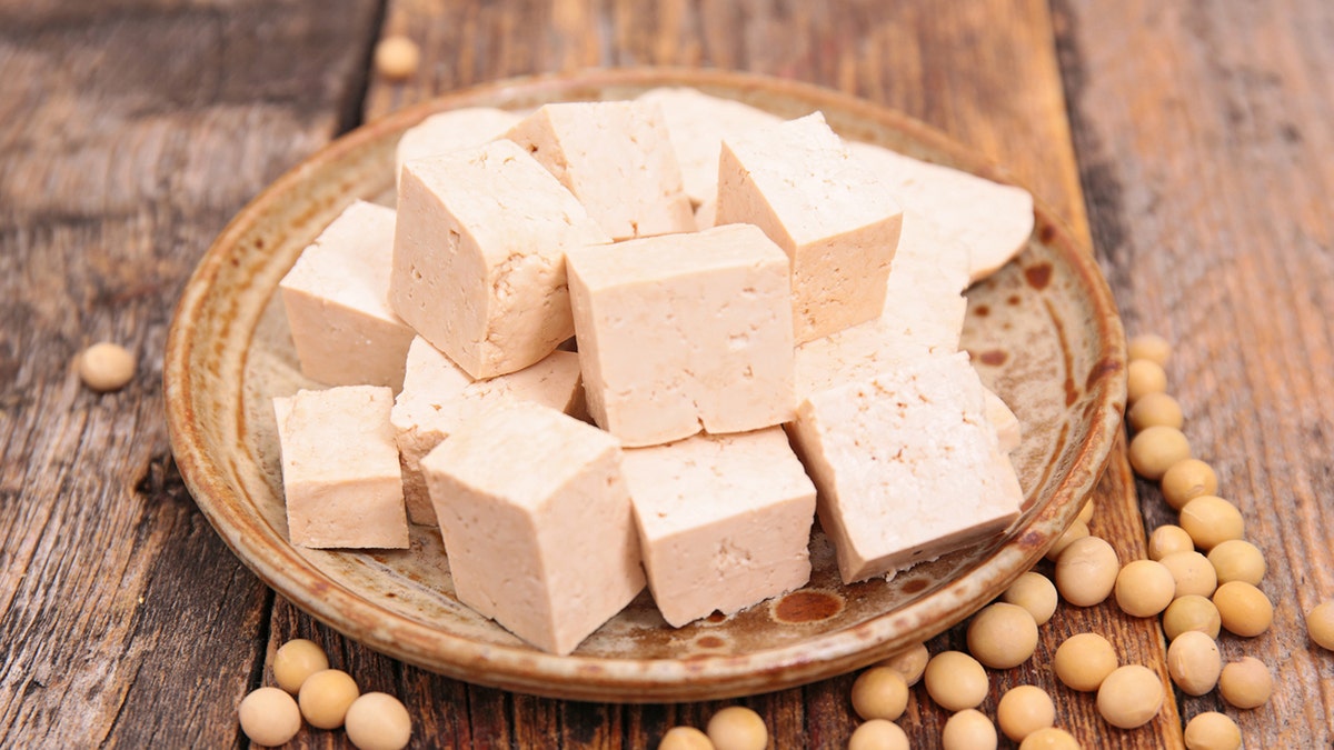 Foto de cuadrados de tofu en un plato con soja al lado.