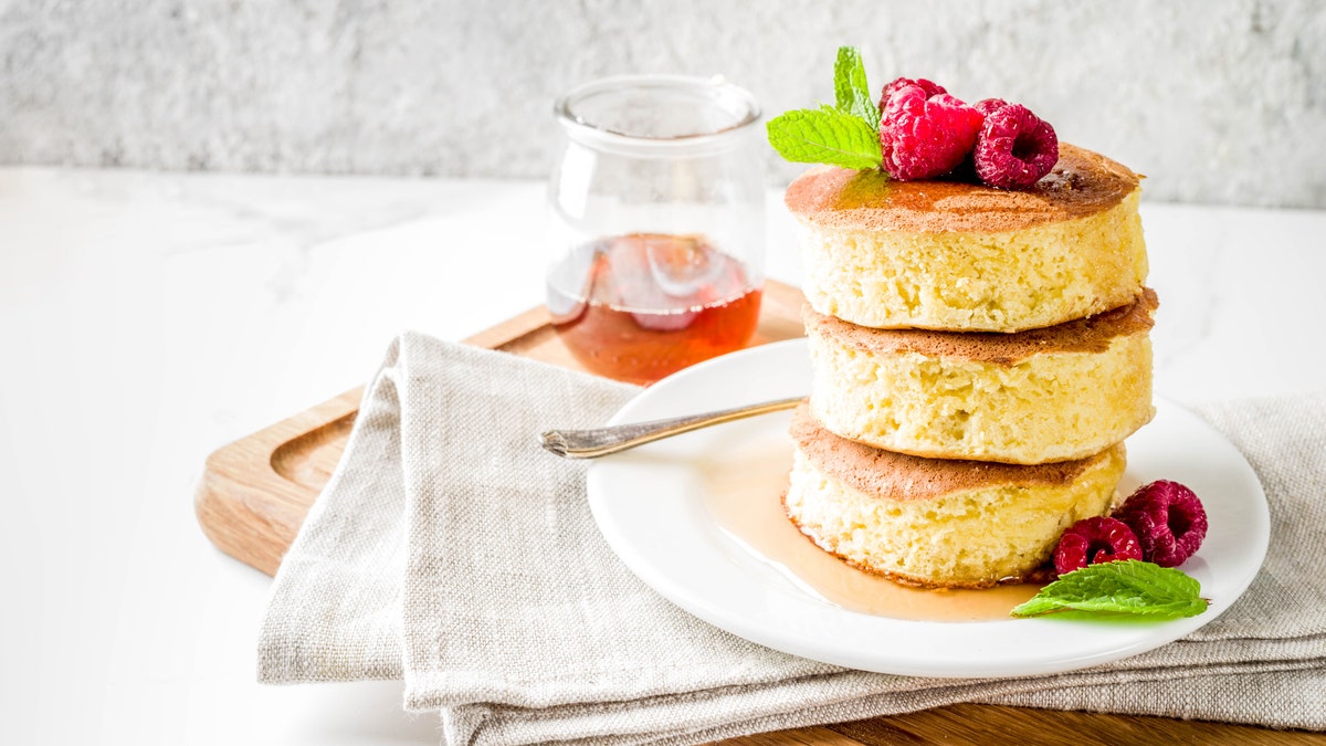 Se expone un plato de tortitas soufflé japonesas con sirope de arce y frambuesas.