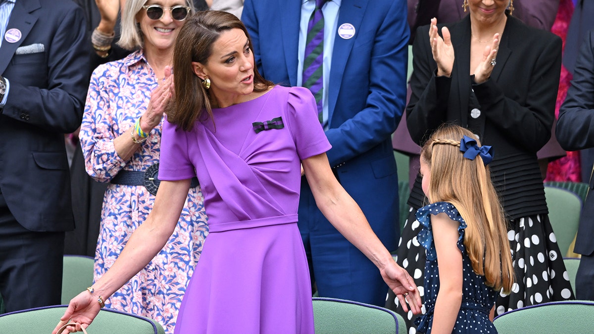 Kate Middleton in a purple dress looks at her daughter Princess Charlotte in polka dots