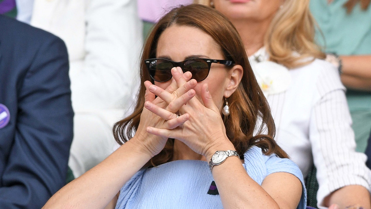 Kate Middleton w niebieskiej sukience zakrywa usta dłońmi, oglądając Wimbledon