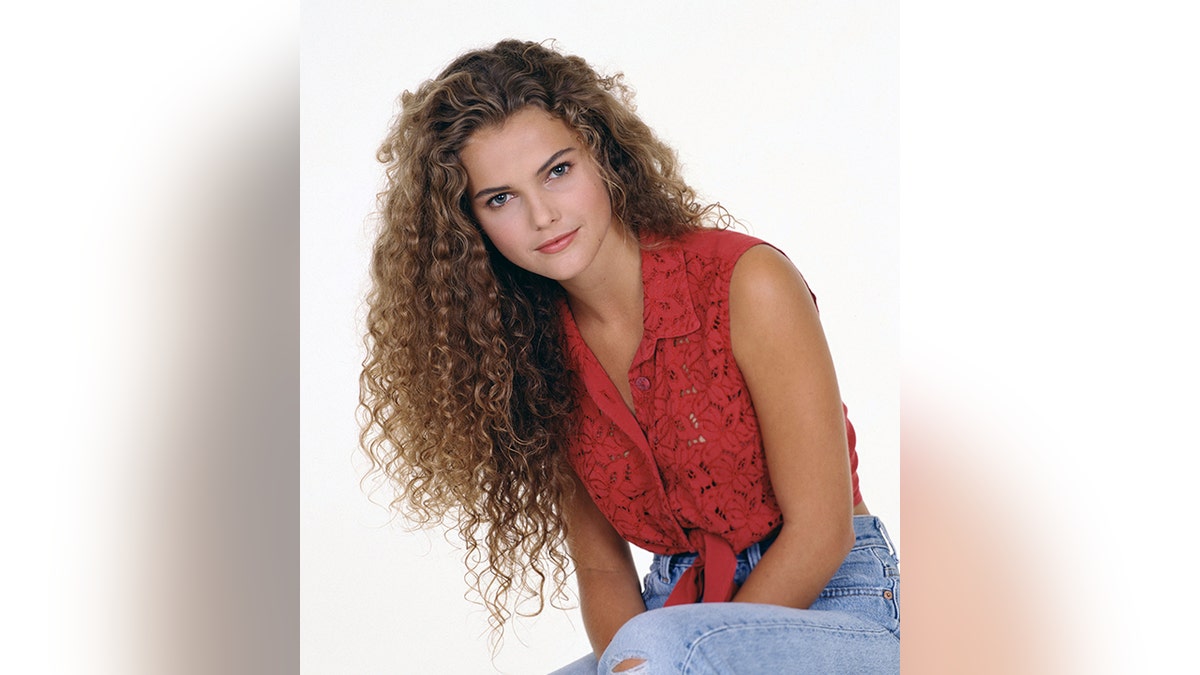 Keri Russell with extremely curly hair in a red top and jeans soft smiling in a portrait