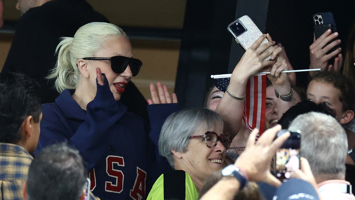Lady Gaga in a blue USA sweatshirt puts up her hands for high fives with fans