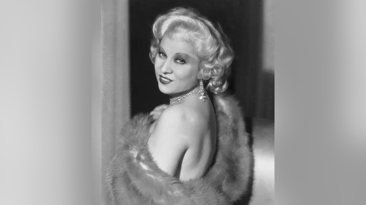 Mae West melihat ke belakang bahunya memamerkan bahunya dalam foto hitam putih