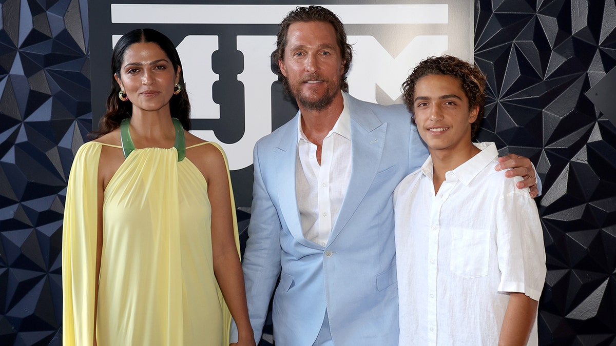 Camila Alves in a yellow dress poses next to Matthew McConaughey in a light blue suit with their son Levi in a white shirt