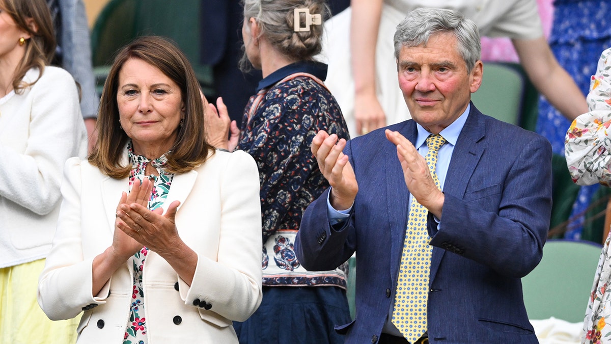 Carole Middleton in a white jacket claps alongside husband Michael Middleton in a blue suit and yellow tie at Wimbledon