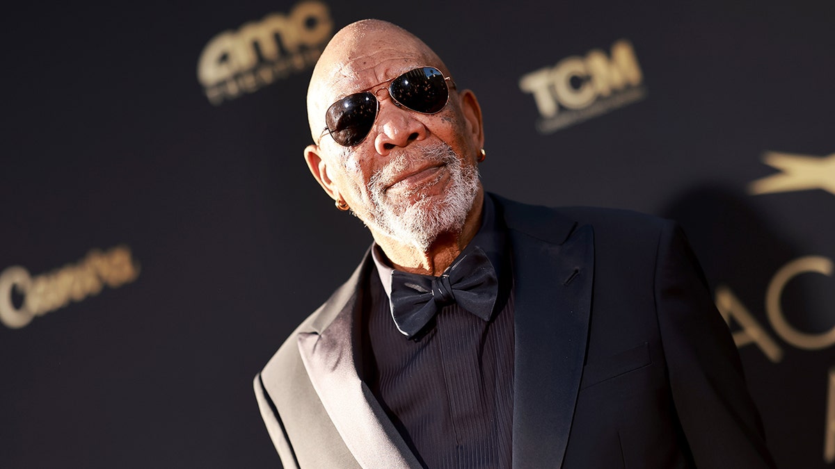 Morgan Freeman in a black suit and dark shades stands tall on the carpet