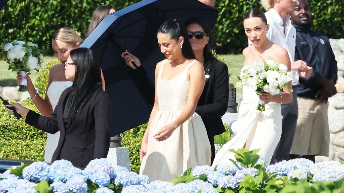 Olivia Culpo's sister Aurora and Sophia Culpo are pictured walking beneath an umbrella to Olivia Culpo's wedding