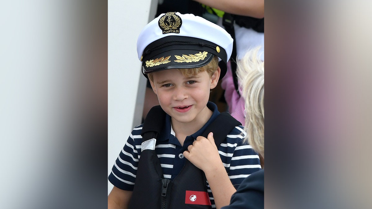 Prince George smiling at the camera while wearing a captain's hat.