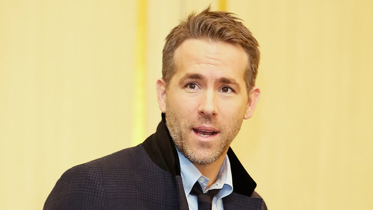 Ryan Reynolds smiles while wearing a black coat