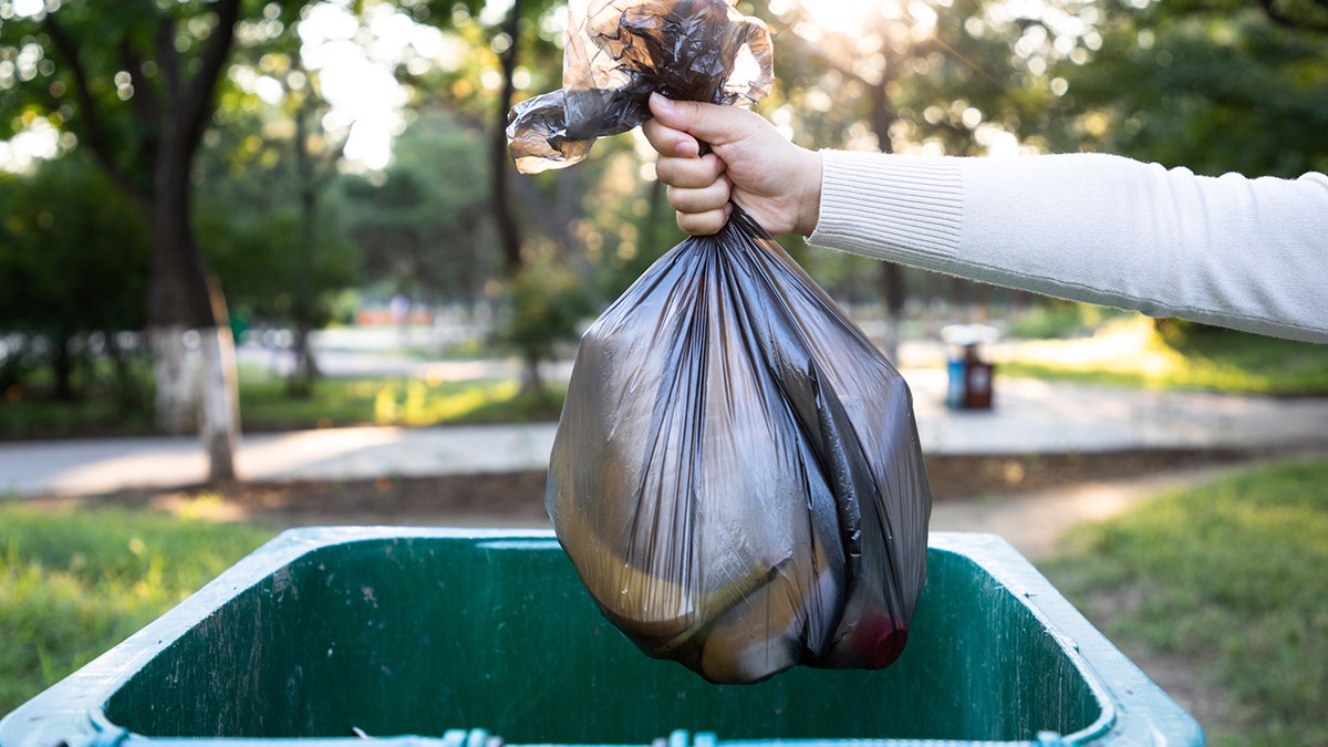 A person throwing a trash bag into garbage bin