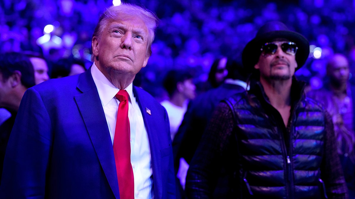 Donald Trump in a blue blazer and red tie in focus in front of Kid Rock