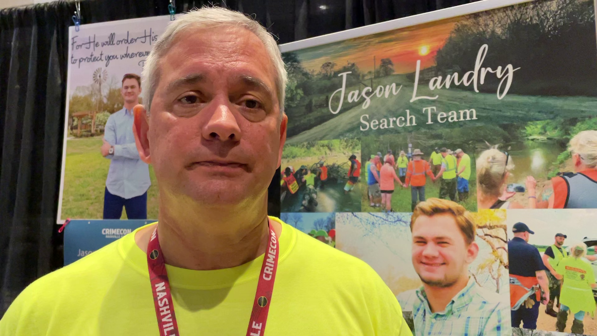 Kent Landry standing in front of a board of pictures of his missing son Jason