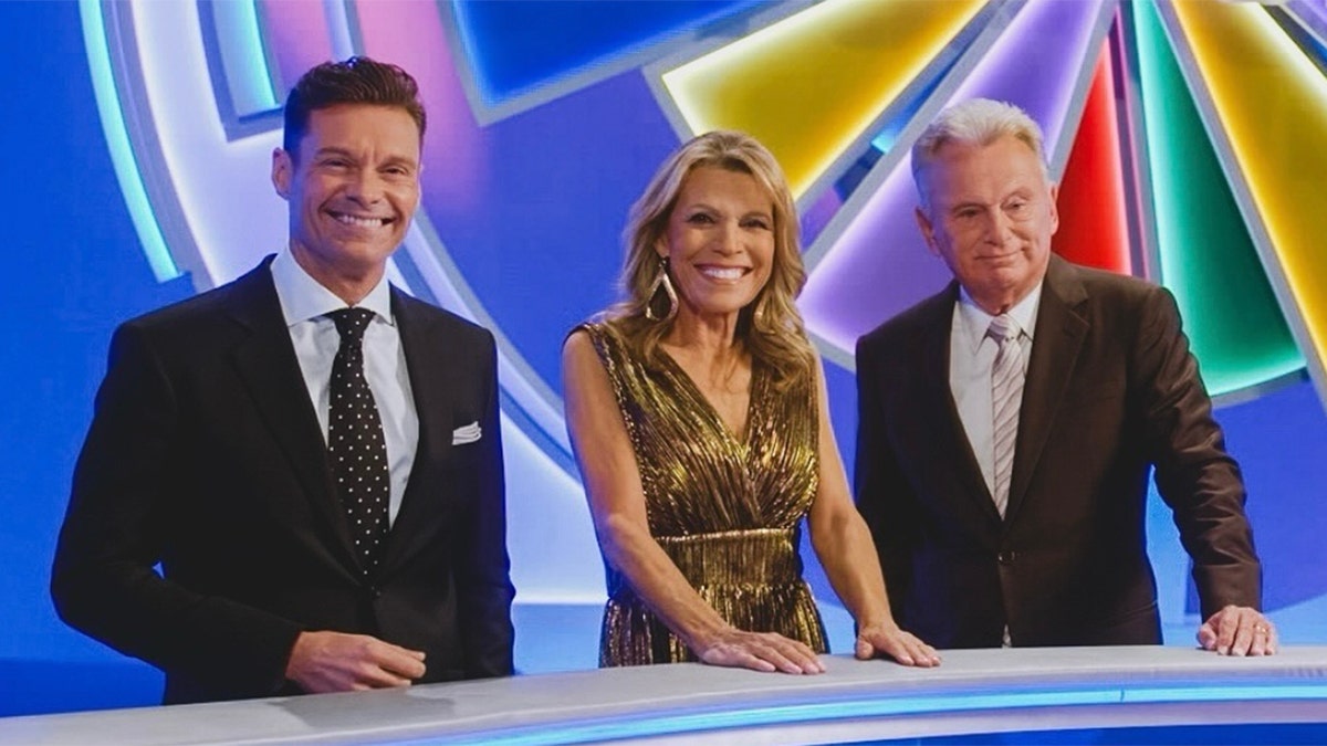 Ryan Seacrest smiles for a photo with Vanna White and Pat Sajak on the set of Wheel of Fortune