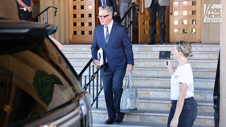 Filmmaker Jenna Rosher (R) films Alec Baldwin departing his hotel