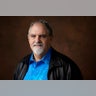 Jon Landau smiling in a black jacket and bright blue shirt