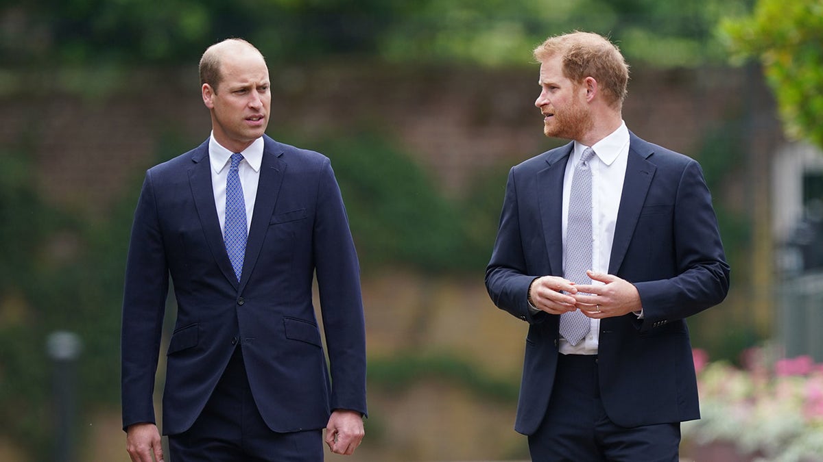 Prince William and Prince Harry in conversation as they wear matching navy blazers and pants.