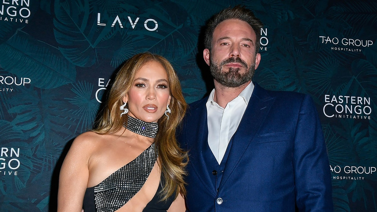 Jennifer Lopez in a cut-out dress smiles on the carpet with Ben Affleck in a blue suit