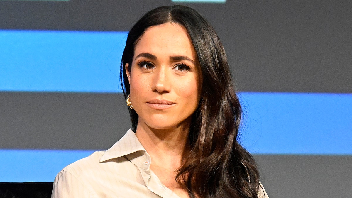 Meghan Markle muy seria con una blusa beige.