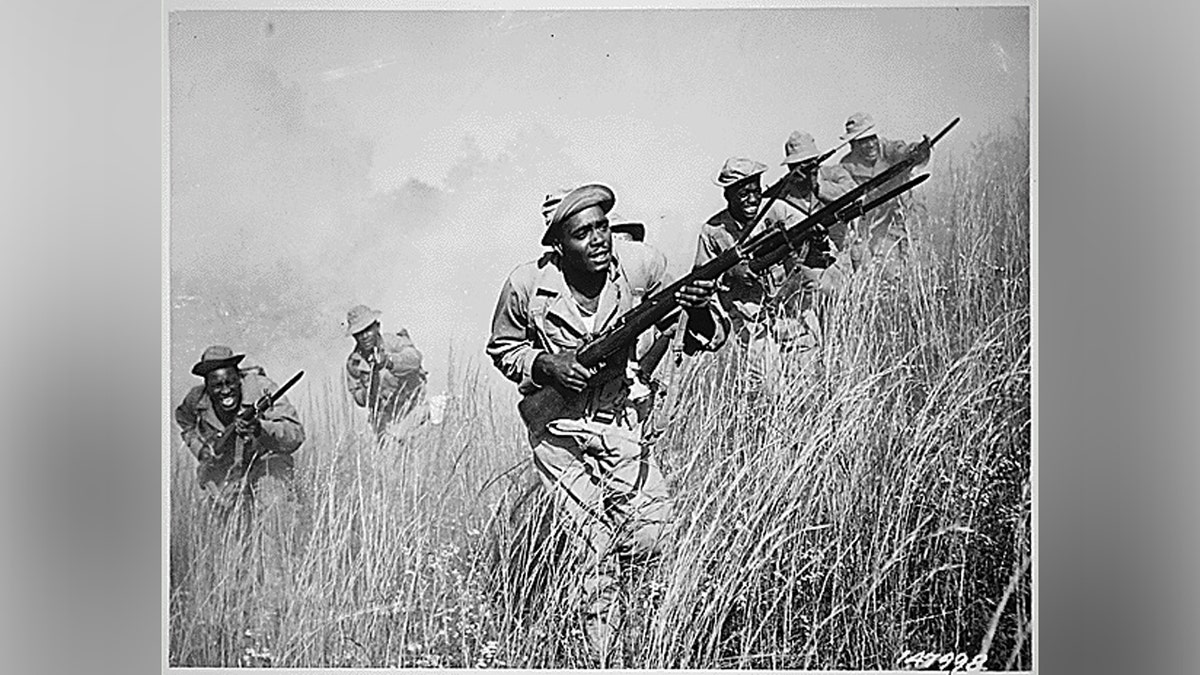 Soldados de la 92ª División de Infantería afroamericana llevan sus armas de fuego por un campo.