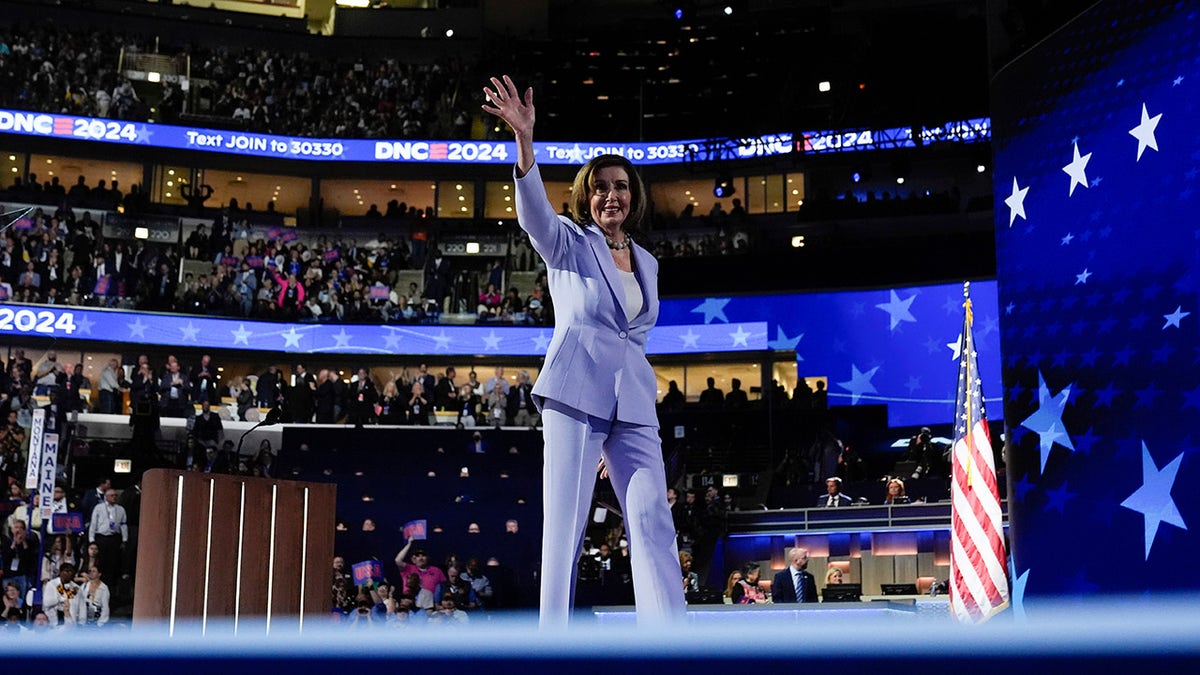 Pelosi wide shot on DNC stage waving in purple pantsuit