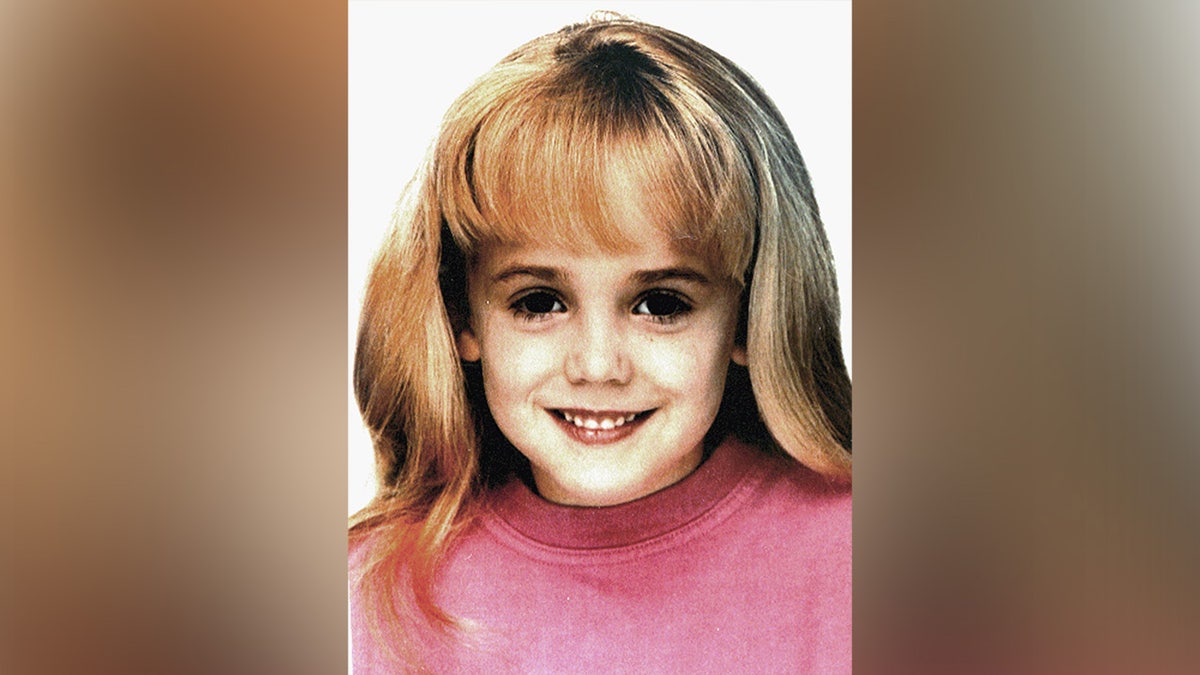 JonBenét Ramsey mengenakan sweter merah muda sambil tersenyum.