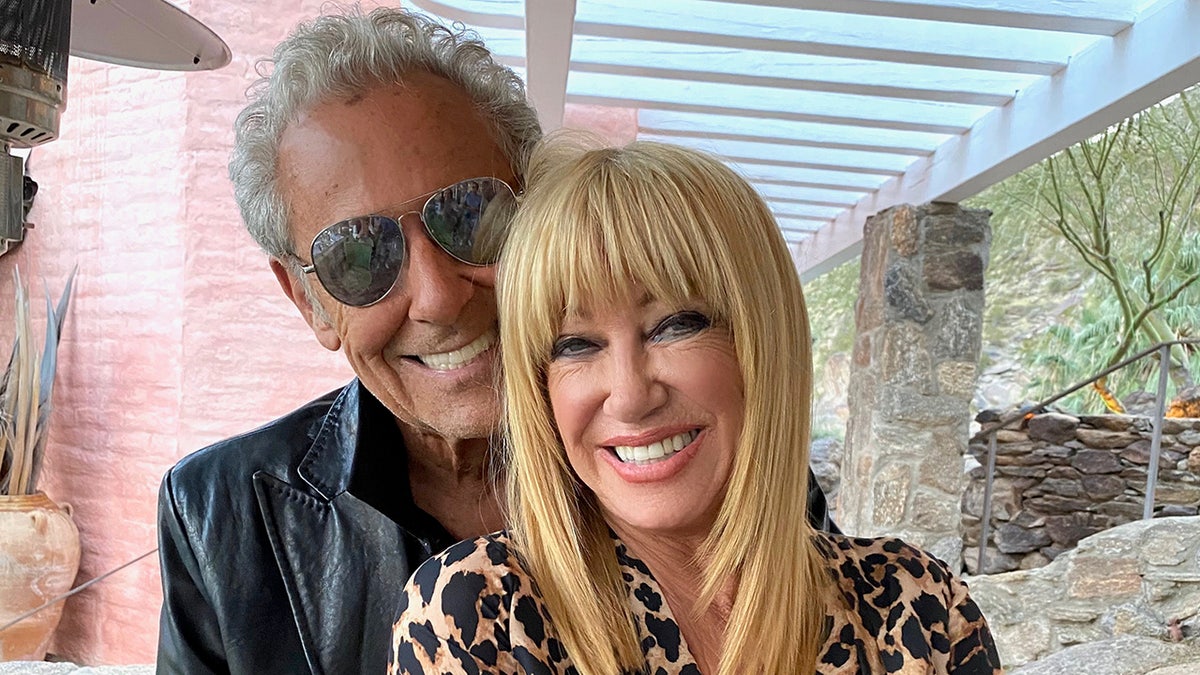 Alan Hamel wearing a leather jacket and smiling holding Suzanne Somers wearing a leopard blouse.
