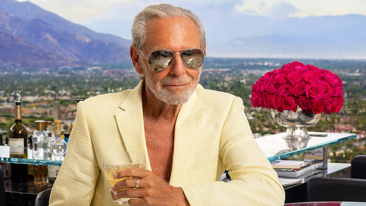 Alan Hamel wearing a beige suit with sunglasses sitting outdoors.