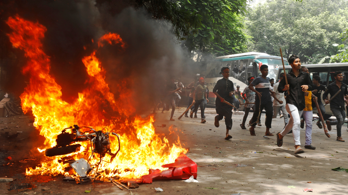 Men run past a burning vehicle inside the Bangabandhu Sheikh Mujib Medical College Hospital, which was set ablaze by protesters, during a demonstration against Prime Minister Sheikh Hasina and her government to demand justice for victims killed in the recent deadly clashes across the country, in Dhaka, Bangladesh, August 4, 2024.