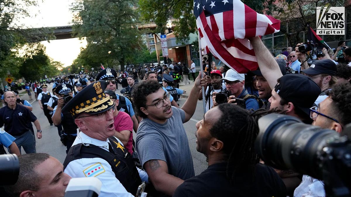 Un hombre con una bandera estadounidense es gritado por manifestantes mientras es desalojado por la policía en Chicago durante una marcha contra el DNC