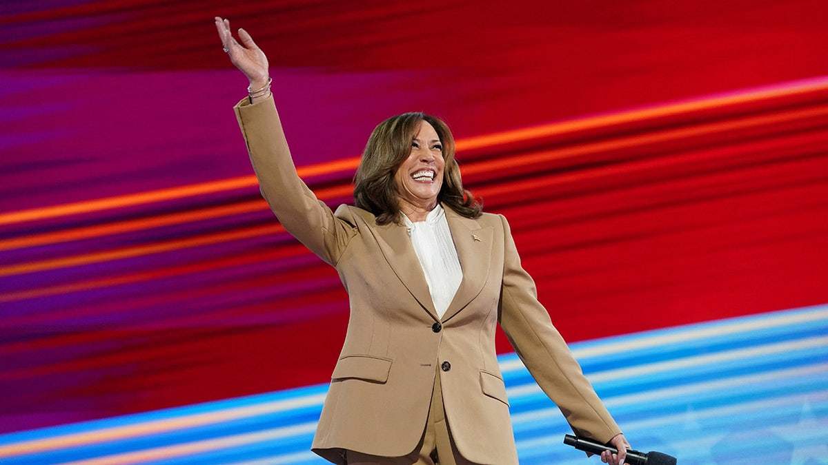 Kamala Harris sonríe ampliamente y agita el brazo en el escenario antes de hablar durante la Convención Nacional Demócrata