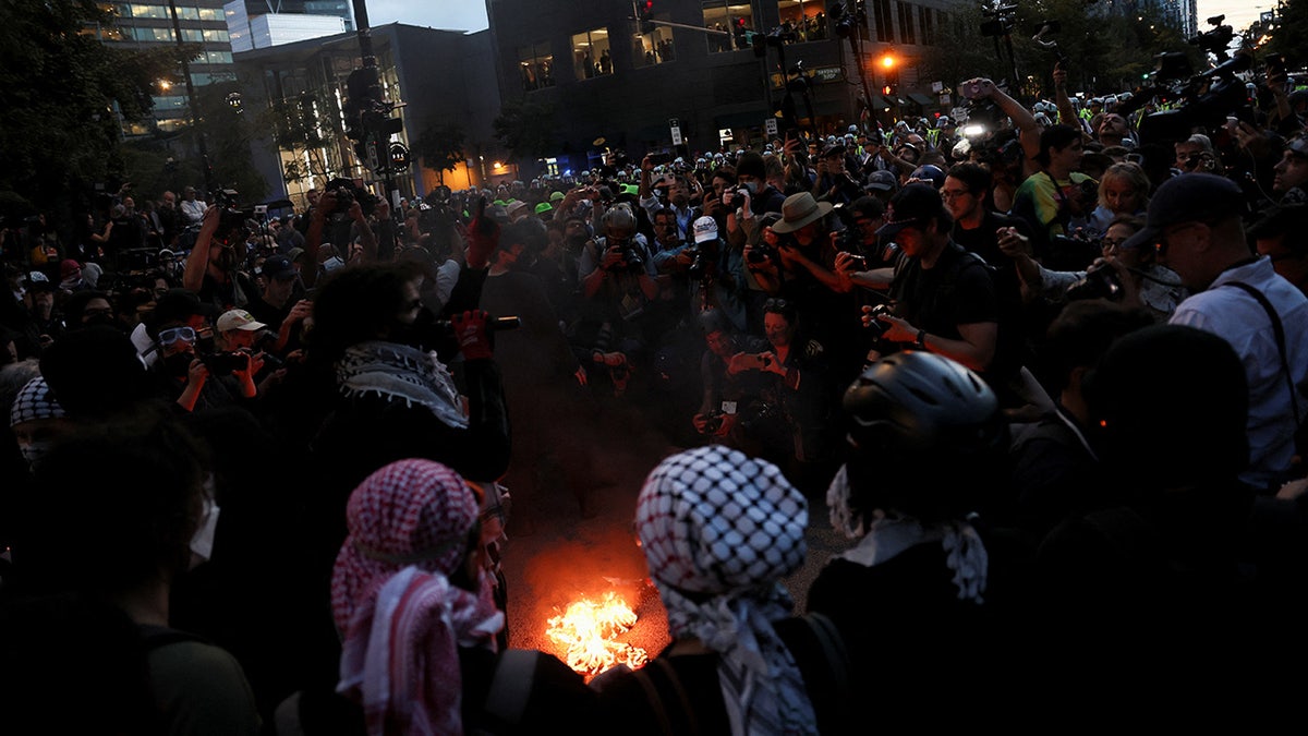 Miembros de los medios de comunicación disparan mientras unos manifestantes prenden fuego a una bandera al margen de la Convención Nacional Demócrata.