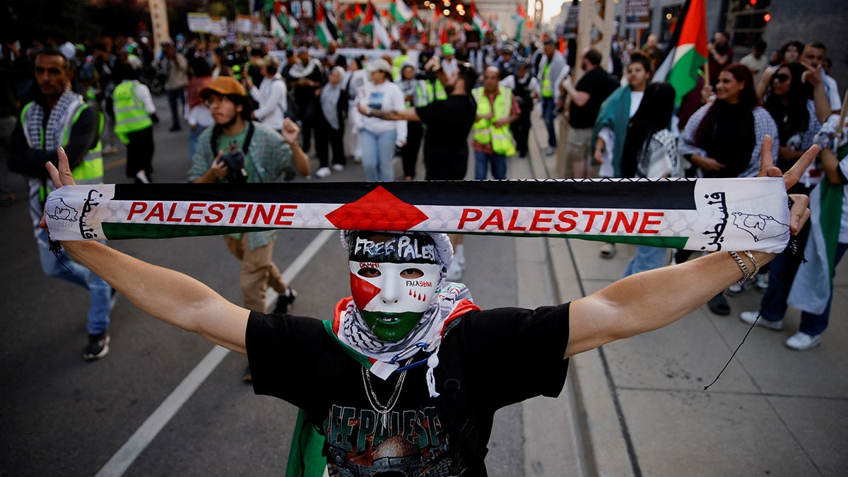 A demonstrator wearing a mask in the colors of the Palestinian flag holds up a scarf during a protest rally in support of Palestinians in the Gaza Strip.