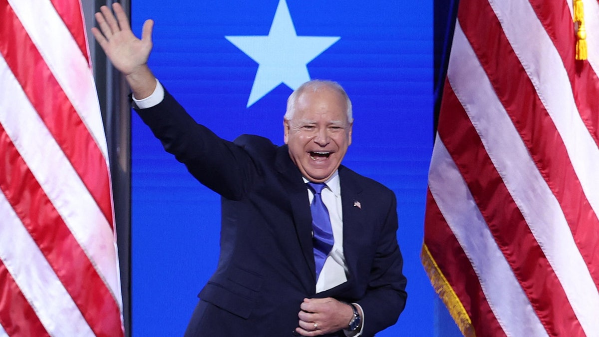 Tim Walz smiling, waving on DNC stage