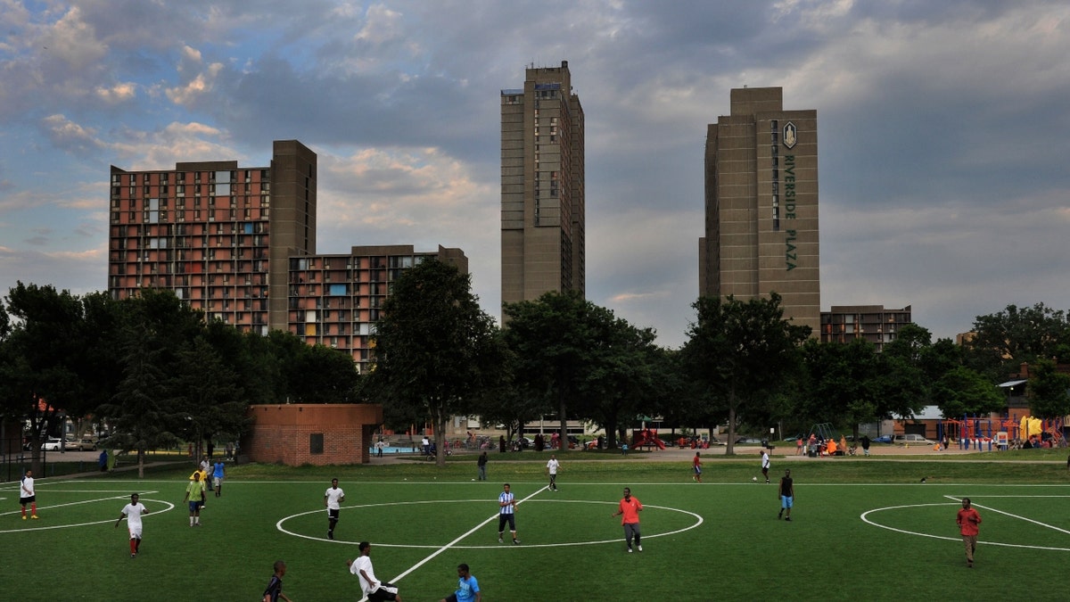 Unos jóvenes juegan al fútbol mientras madres y padres socializan y crían a sus hijos en el Parque Currie, junto al complejo de apartamentos Cedar-Riverside, que alberga principalmente a somalíes desplazados aquí desde principios de los años 90 por la guerra civil de su país, el 30 de junio de 2011, en Minneapolis, MN. 