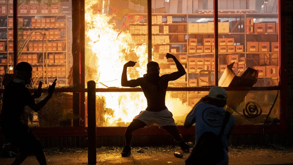 Shirtless man stands in front of burning store window