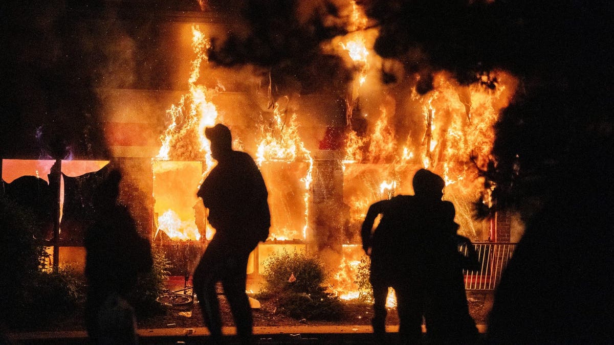 Flames engulf and AutoZone store as people move in front of the fire