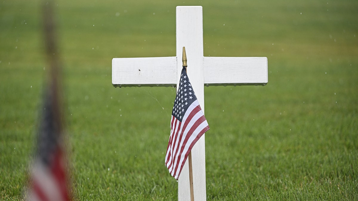 An American flag at a veteran's grave, marked by a cross.