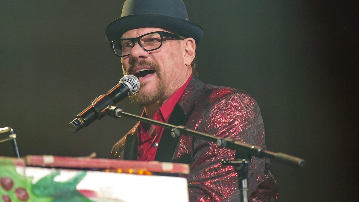 Phil Vassar in a red and black suit and black top hat performing behind the piano