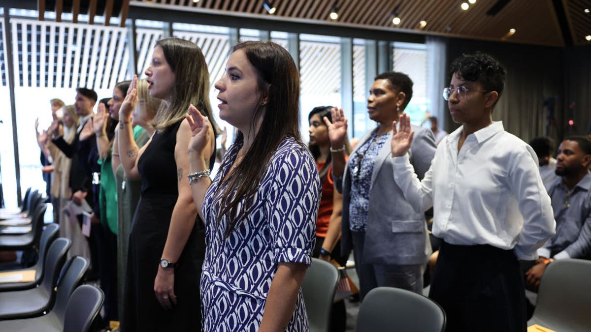 People raise their hands as they take the Oath of Allegiance during a Naturalization Ceremony at the Stavros Niarchos Foundation Library on July 02, 2024, in New York City. (Photo by Michael M. Santiago/Getty Images)