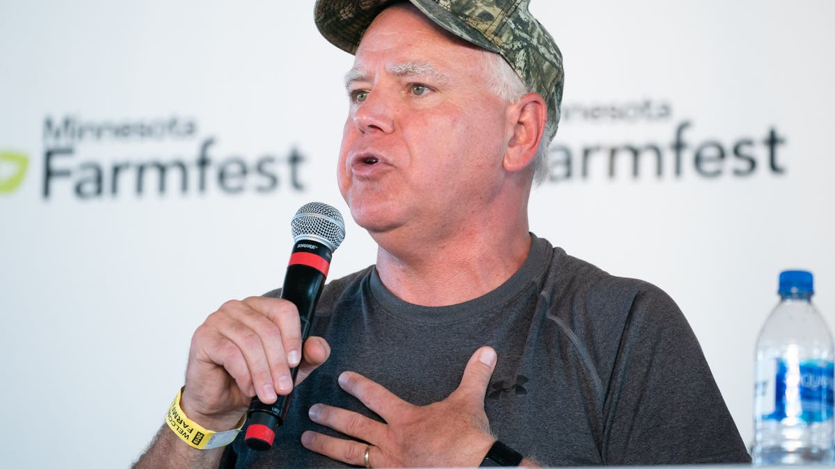 Tim Walz in 2018 in camo baseball cap, holding microphone