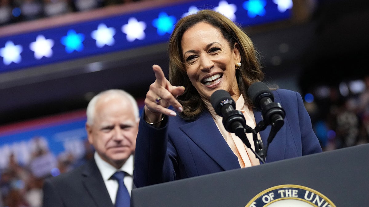 Harris at campaign event pointing, Tim Walz behind her