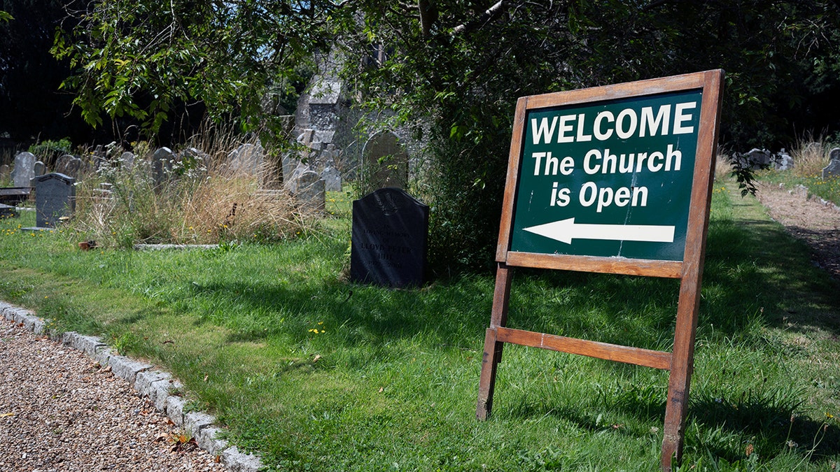 Cartel que dice "BIENVENIDOS La iglesia está abierta" con una flecha en la iglesia de Santa María en Inglaterra