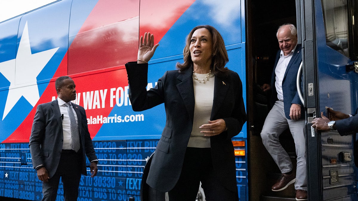 Kamala Harris melambaikan tangan saat Gubernur Tim Walz keluar dari bus